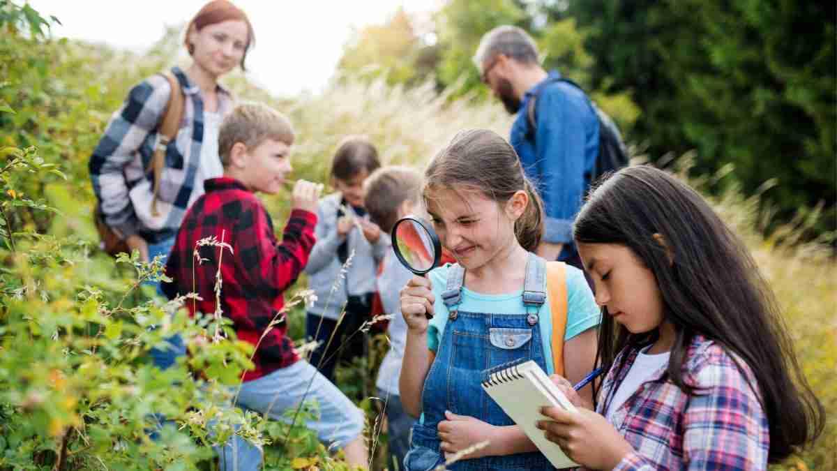 Eine Gruppe von Kindern untersucht Pflanzen in der Natur mit Lupe und Notizbuch.