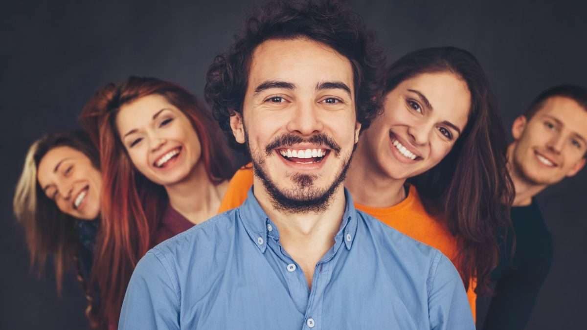 Eine Gruppe von fünf Personen lächelt in die Kamera, während sie hintereinander stehen.