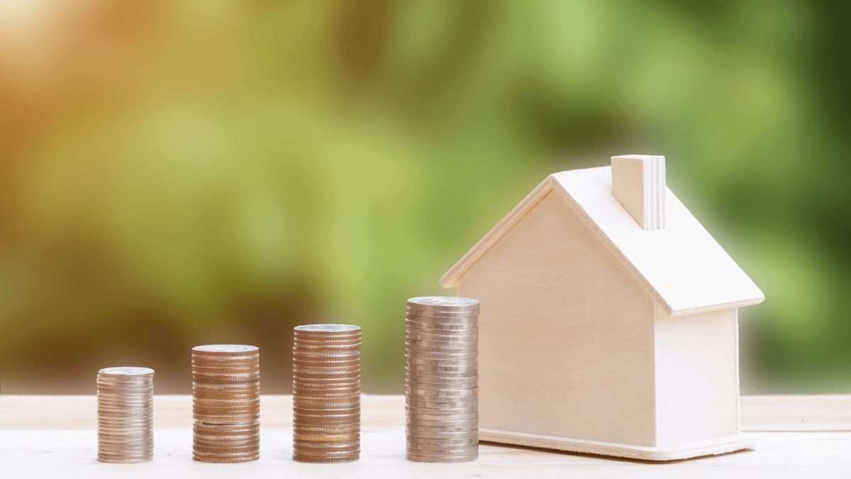 Ein Holzhaus neben gestapelten Münzen in verschiedenen Höhen auf einem Tisch.