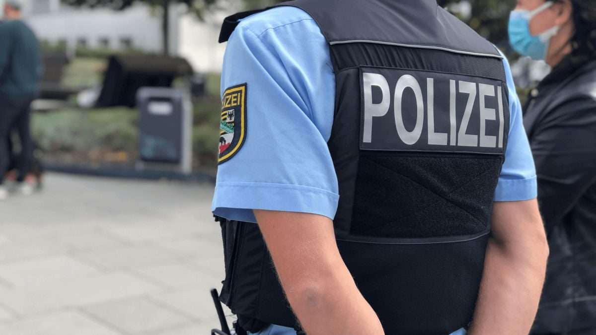 Polizist mit der Aufschrift 'Polizei' auf der Rückseite seiner Schutzweste, trägt eine Gesichtsmaske.