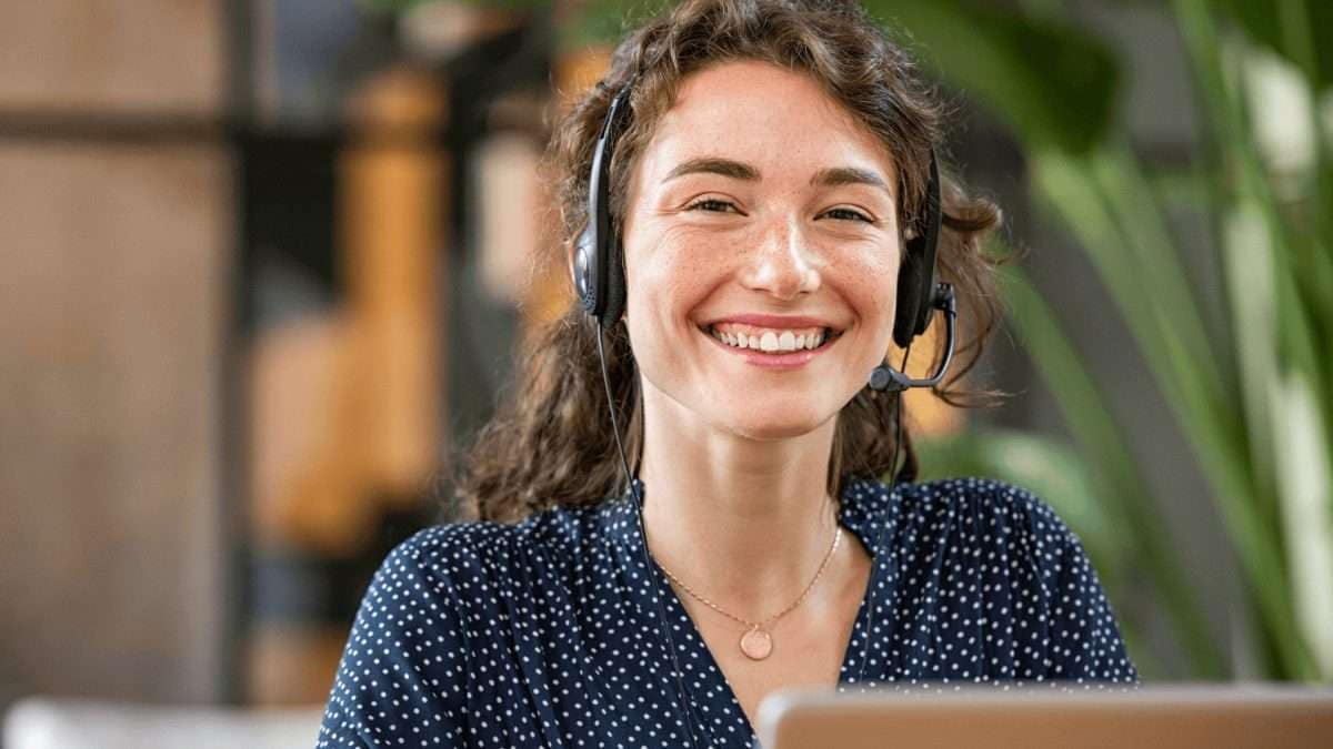 Lächelnde Frau mit Headset, die vor einem Laptop sitzt und in einem modernen Büro arbeitet.