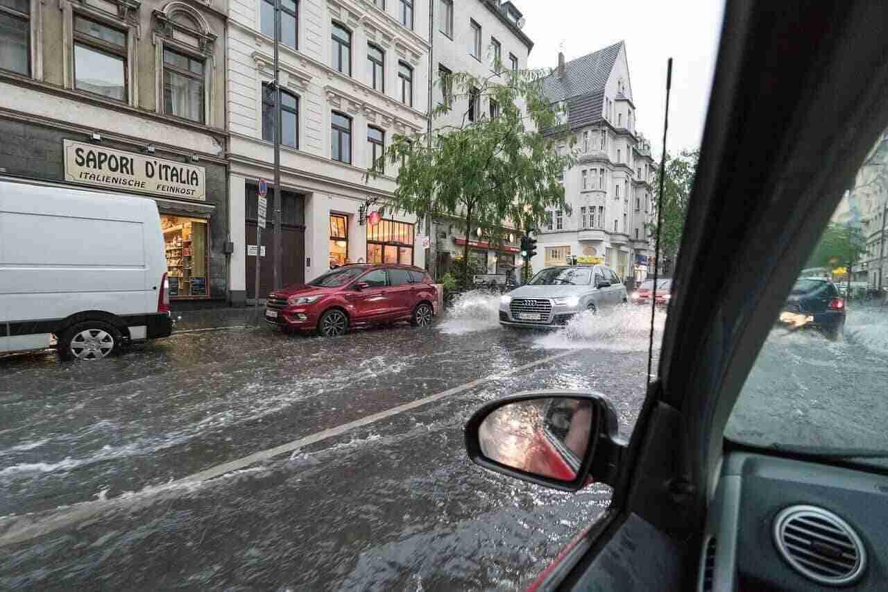 Überschwemmte Straße in Köln mit mehreren Fahrzeugen, die durch Wasser fahren.