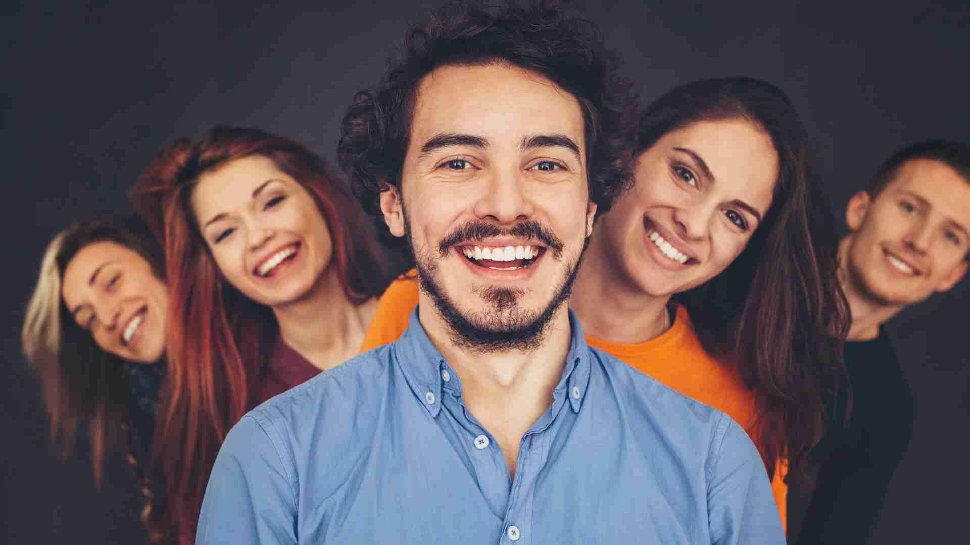 Fünf lächelnde Personen stehen in einer Reihe, wobei der Mann in der Mitte im Vordergrund ist.