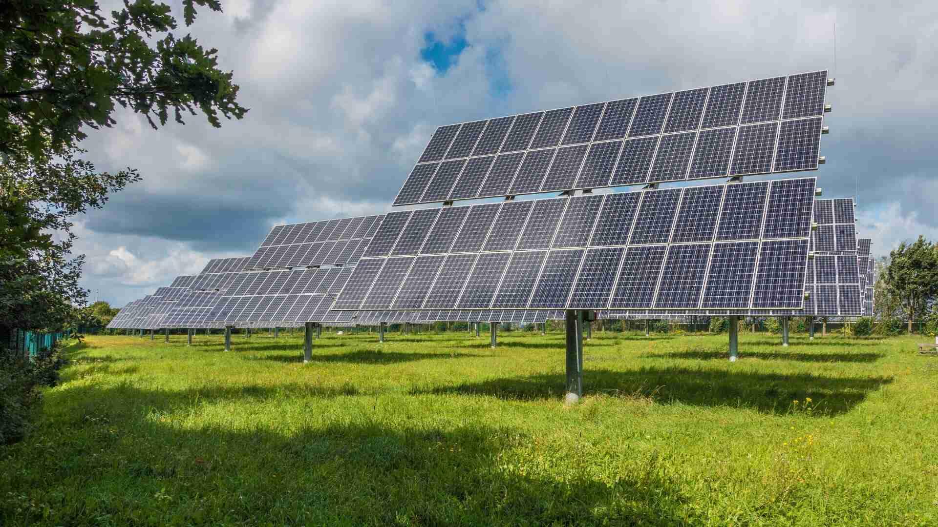 Reihe von Solarpanelen auf einer Wiese, aufgestellt in einem geraden Muster unter einem bewölkten Himmel.