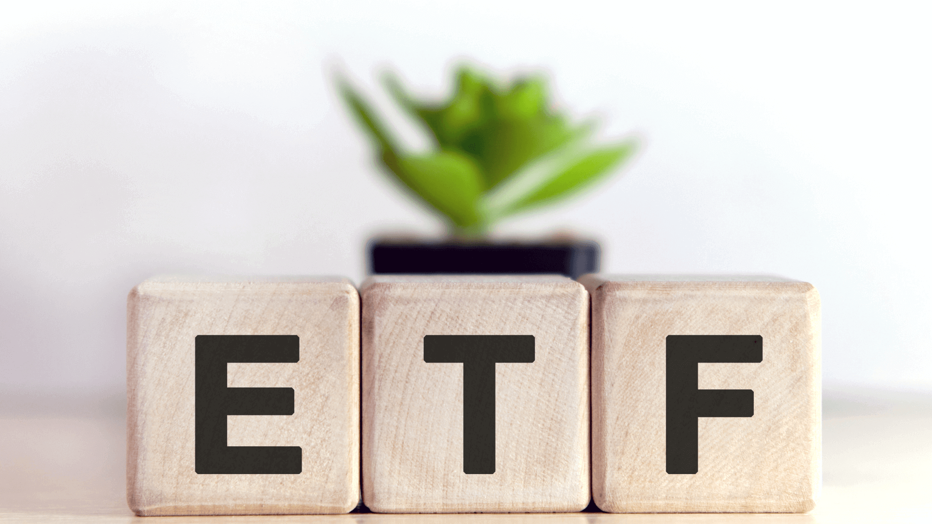 Holzwürfel mit den Buchstaben ETF in schwarzer Schrift, im Hintergrund eine Pflanze.