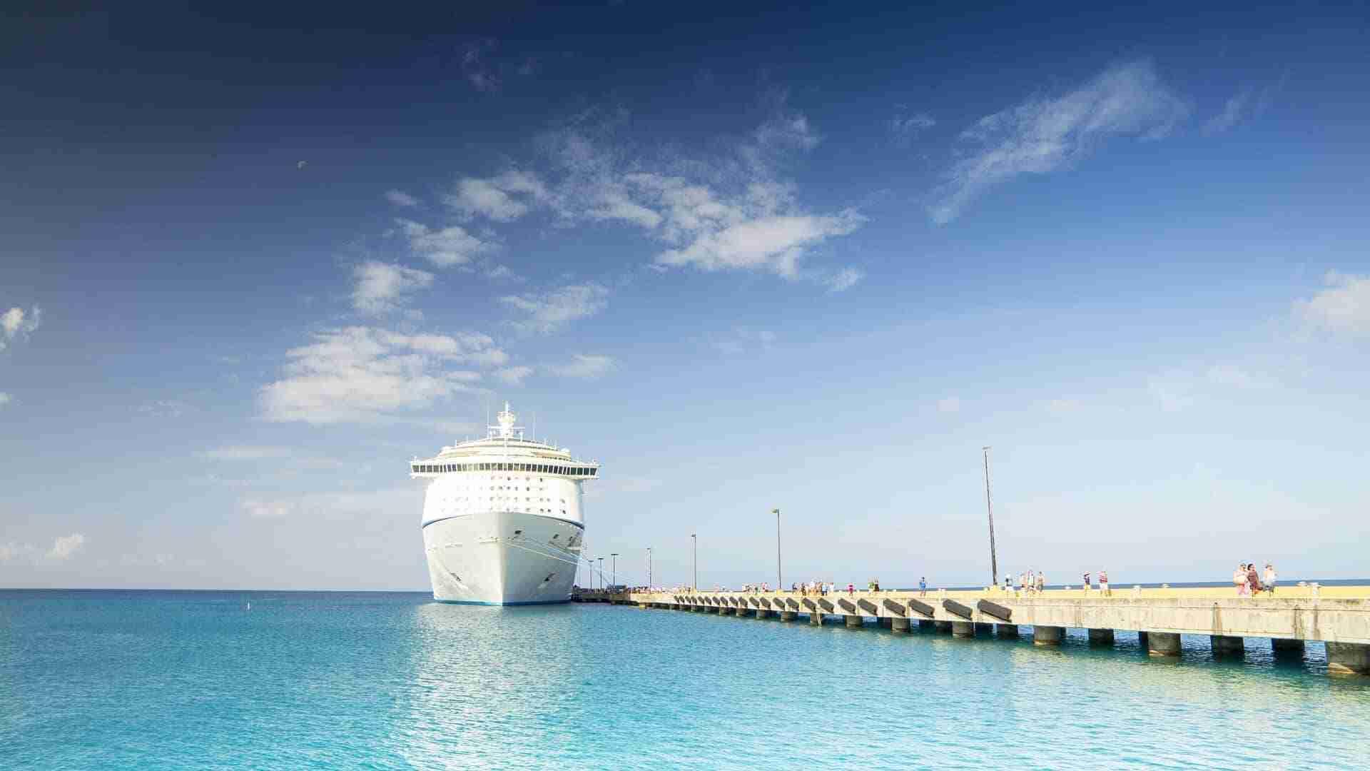Ein großes Kreuzfahrtschiff liegt am Pier mit klarem Wasser und blauem Himmel im Hintergrund.