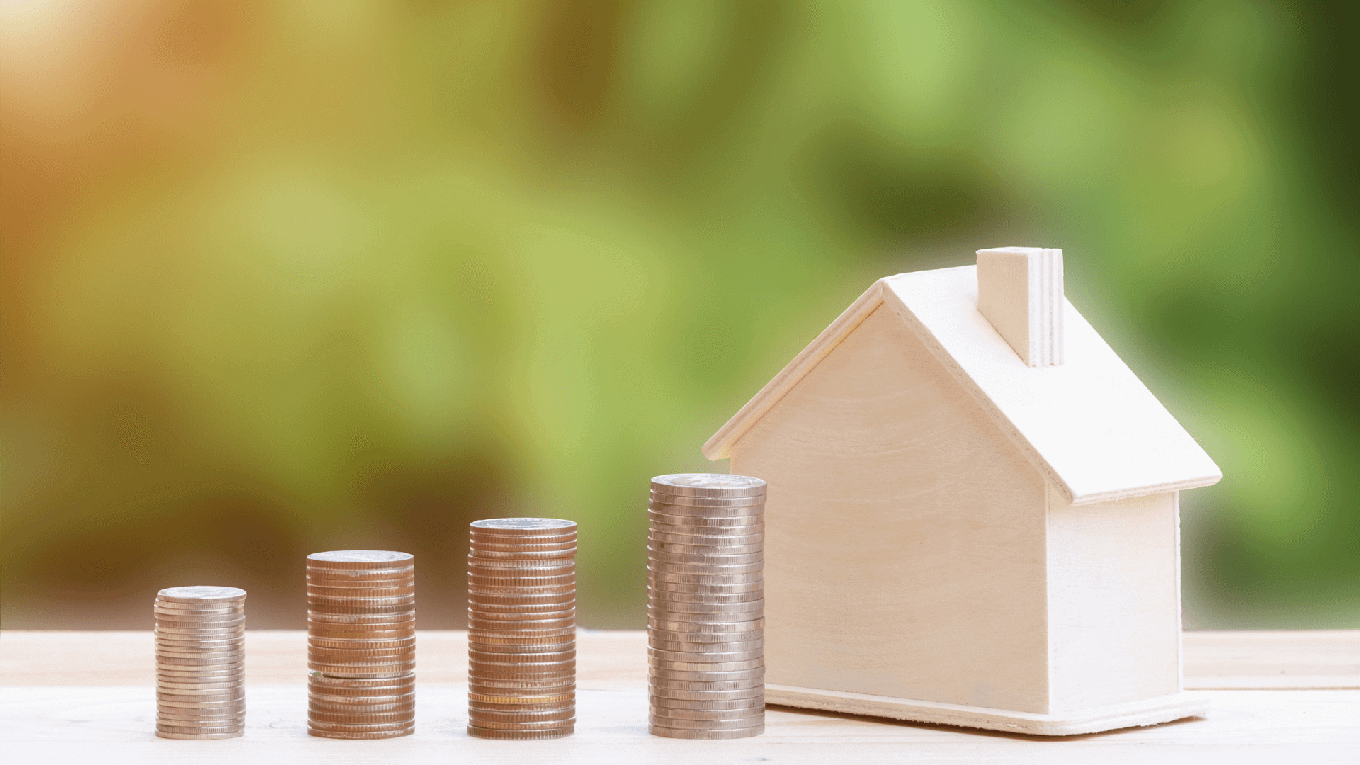 Ein Holzhaus neben gestapelten Münzen in verschiedenen Höhen auf einem Tisch.