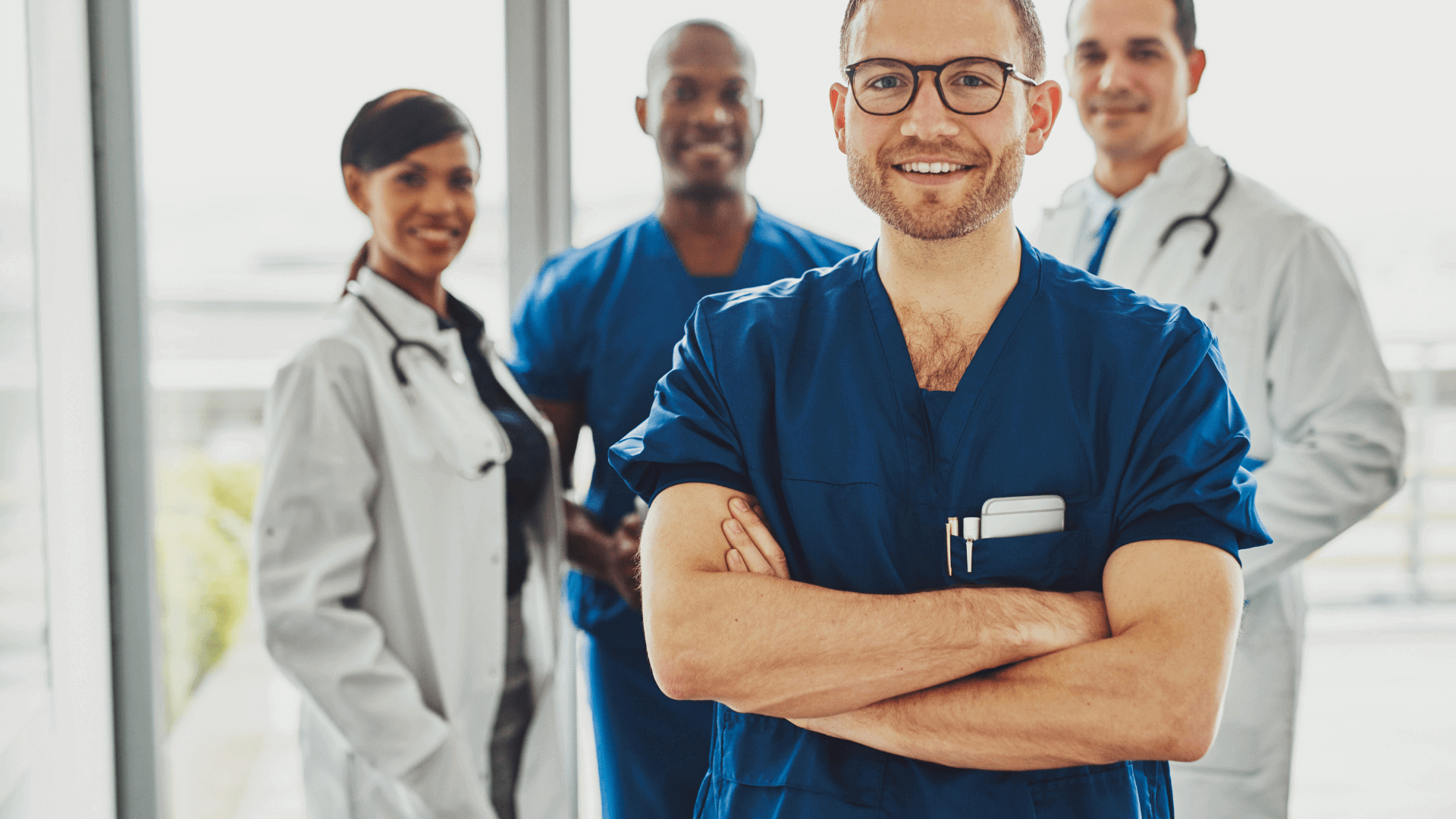 Vier medizinische Fachkräfte, darunter ein Mann in blauem Kittel und Brille, stehen lächelnd zusammen.