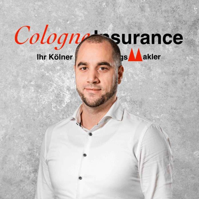 Porträt eines Mannes mit kurzem Bart, der in einem weißen Hemd vor einer grauen Wand steht.