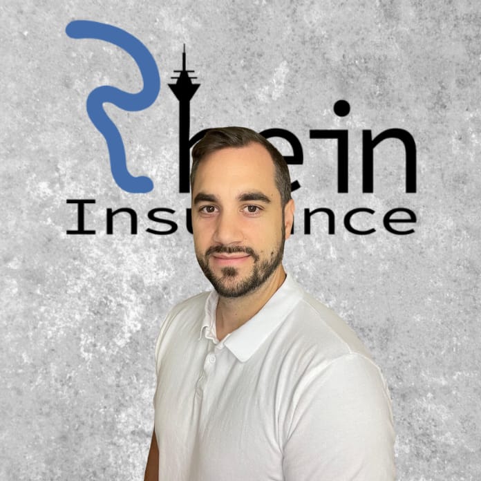 Patrick Warych von Rhein Insurance vor einem grau strukturierten Hintergrund mit blauem Logo, bereit für Beratung zu Baufinanzierung und Immobilienfinanzierung.