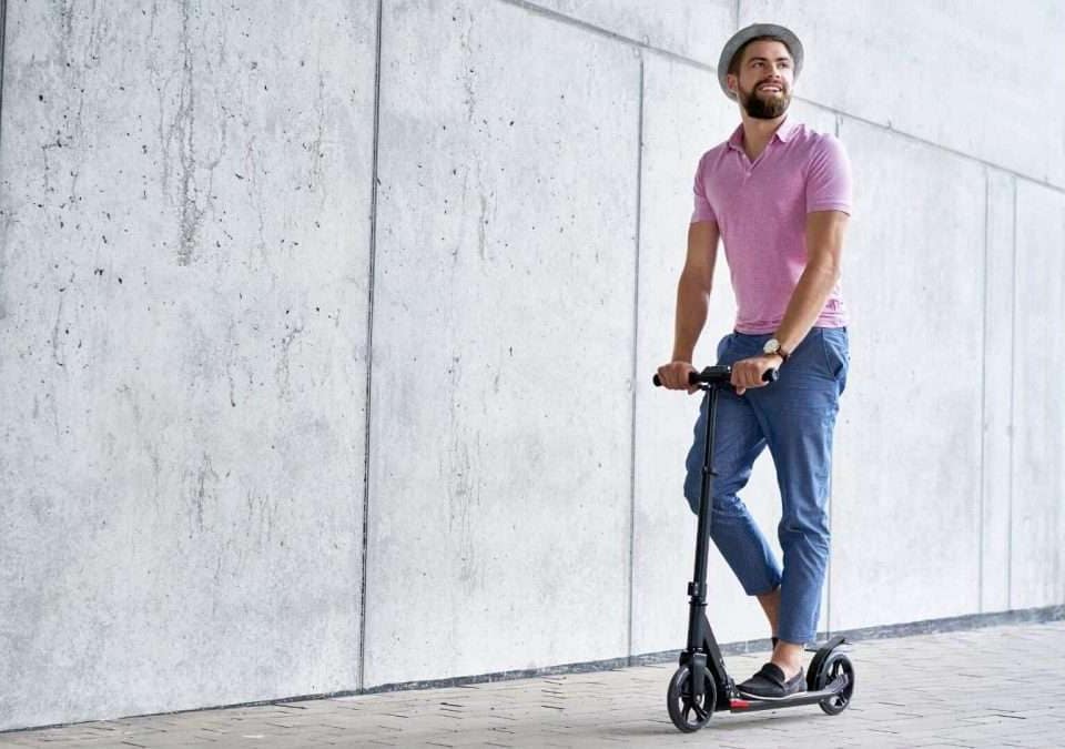 Mann in rosa Hemd und Hut fährt auf einem E-Scooter in einer urbanen Umgebung.