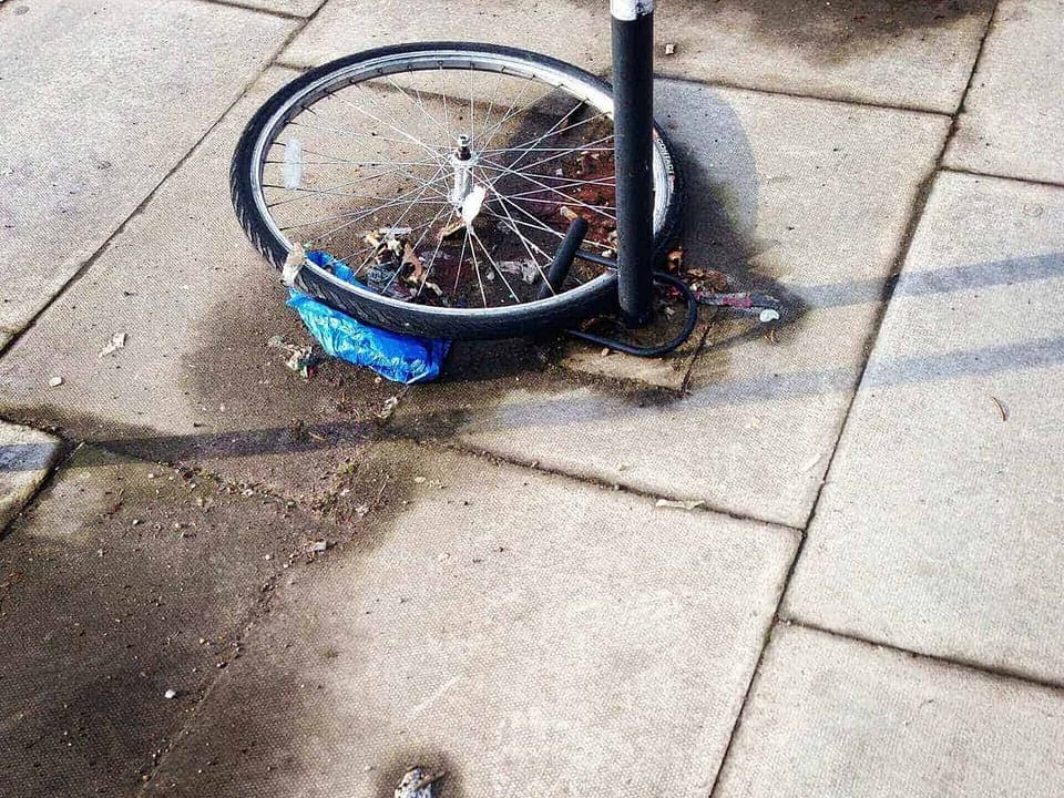 Ein defektes Fahrradrad mit einem blauen Tuch, das an einem Laternenpfahl befestigt ist.