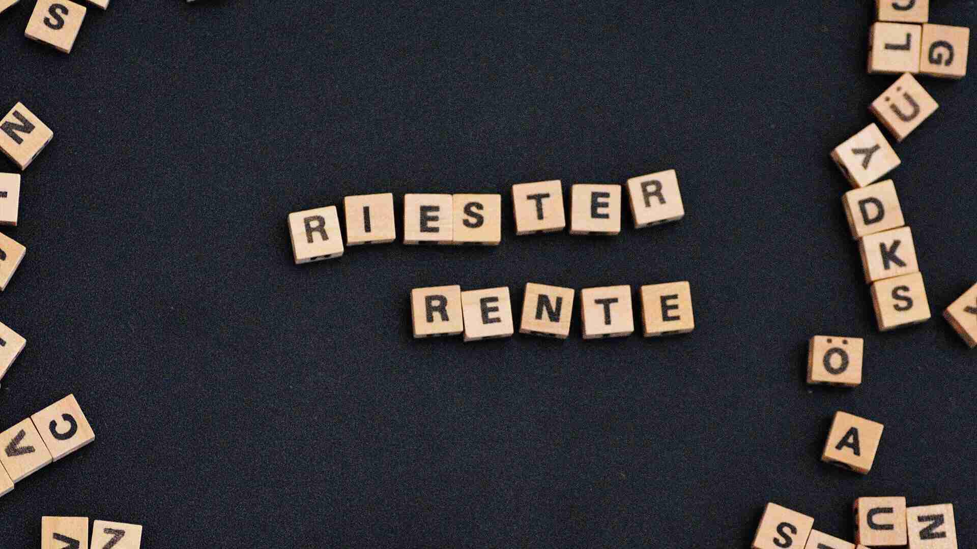 Holzbuchstaben auf einem schwarzen Hintergrund, die die Wörter 'Riester' und 'Rente' bilden.