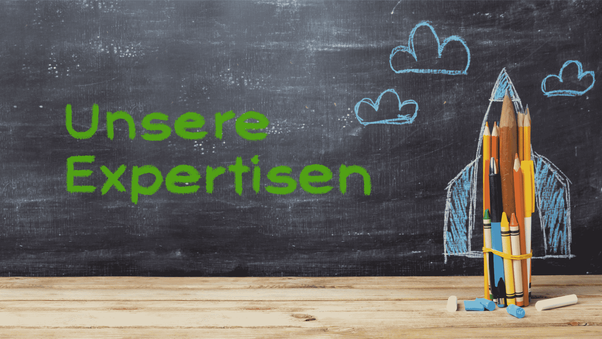 Buntstifte und Kreide auf einer Tafel mit dem Text 'Unsere Expertisen' in grüner Schrift.
