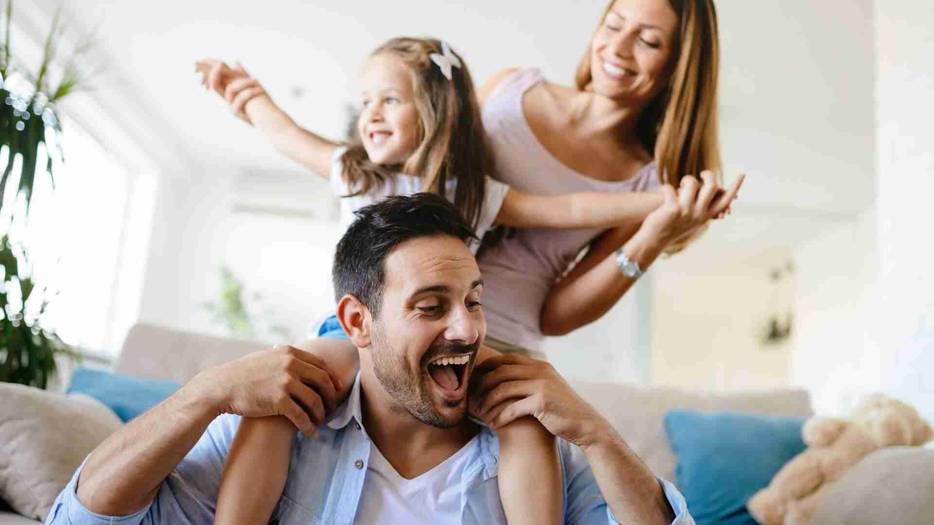 Eine Familie mit einem Mann, einer Frau und einem Kind, das auf den Schultern des Mannes sitzt und lacht.