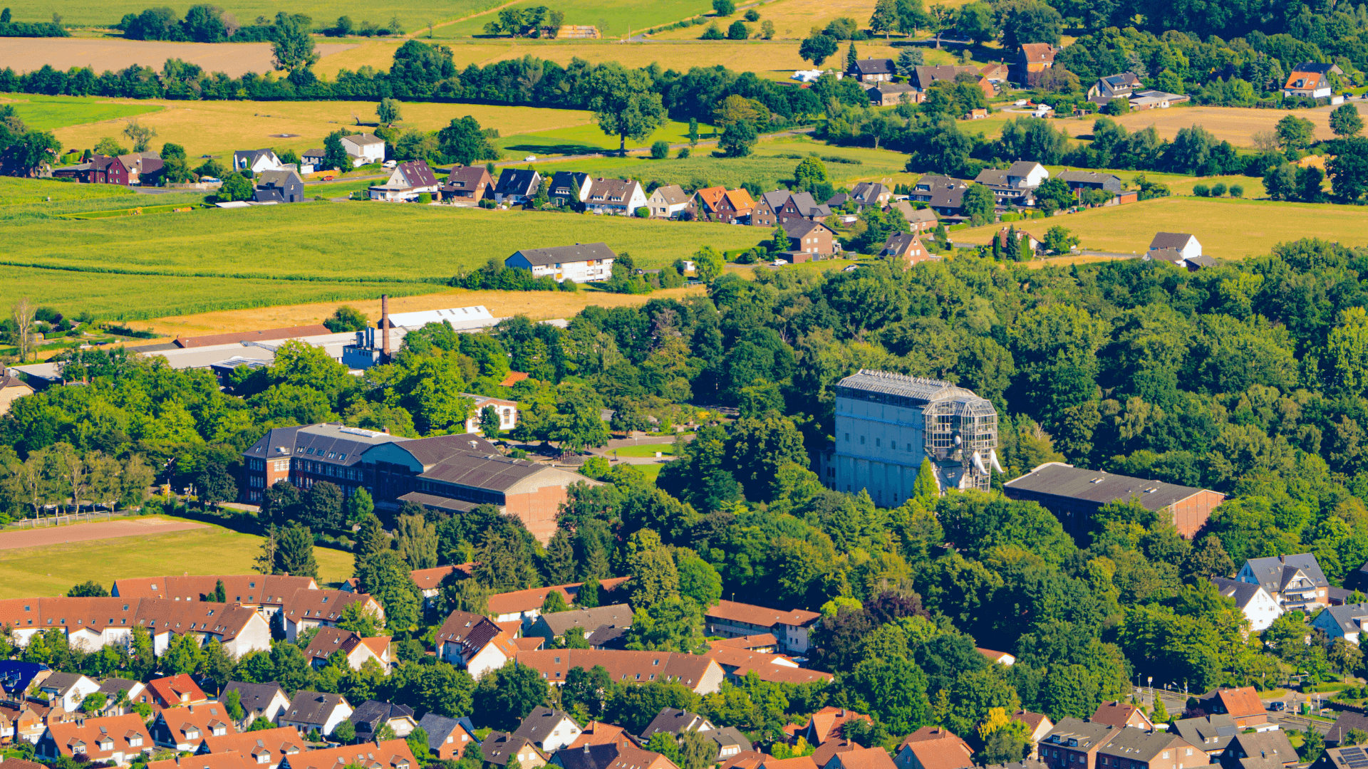 Luftaufnahme einer ländlichen Landschaft mit Häusern, Feldern und Bäumen.