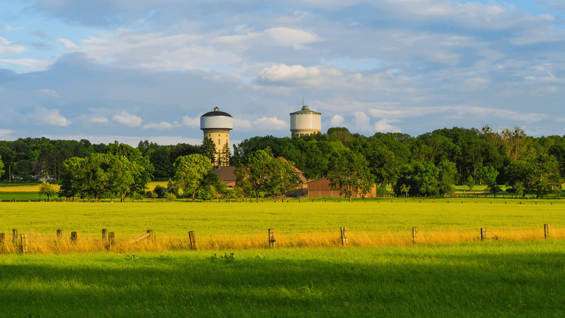 Zwei Wassertürme in einer ländlichen Landschaft mit grünen Wiesen und Bäumen im Hintergrund.