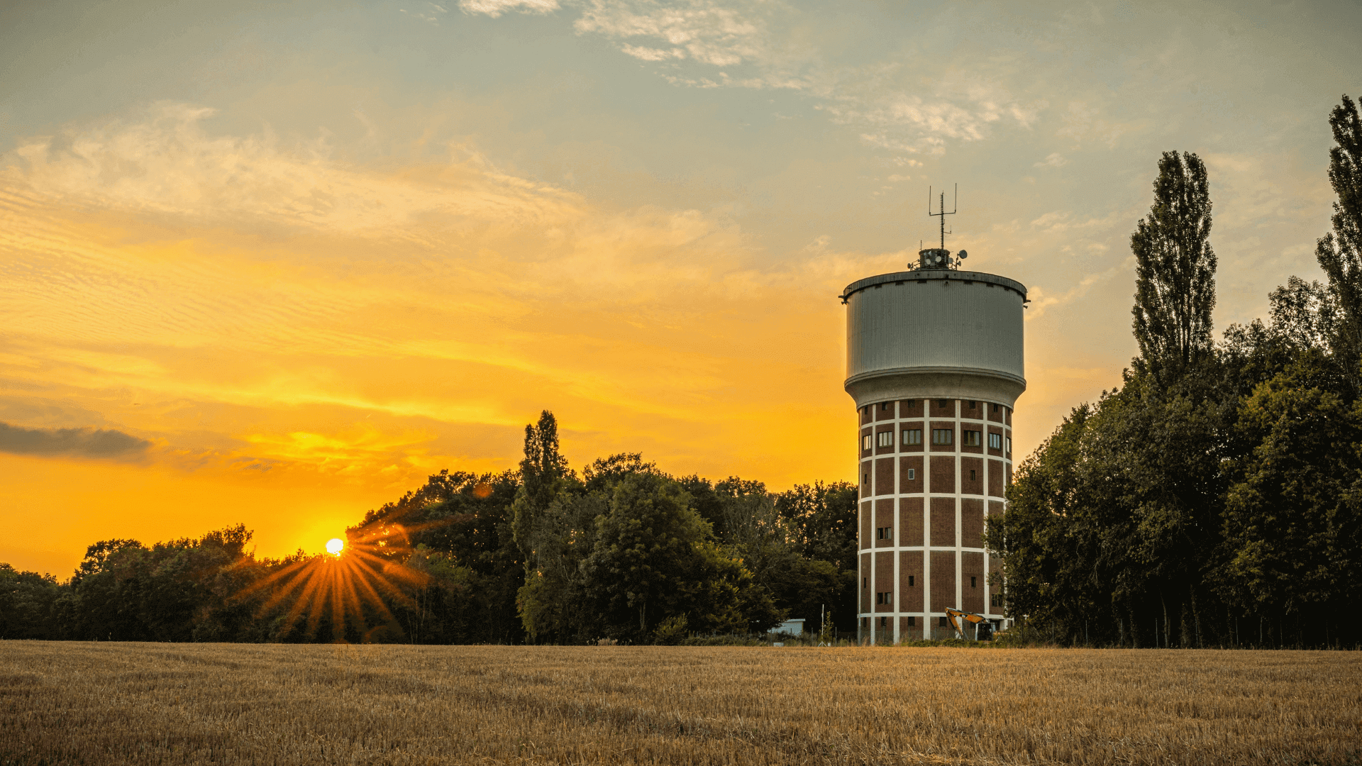 Wasserturm mit einem runden oberen Teil und Ziegelmauerwerk vor einem Sonnenuntergang.