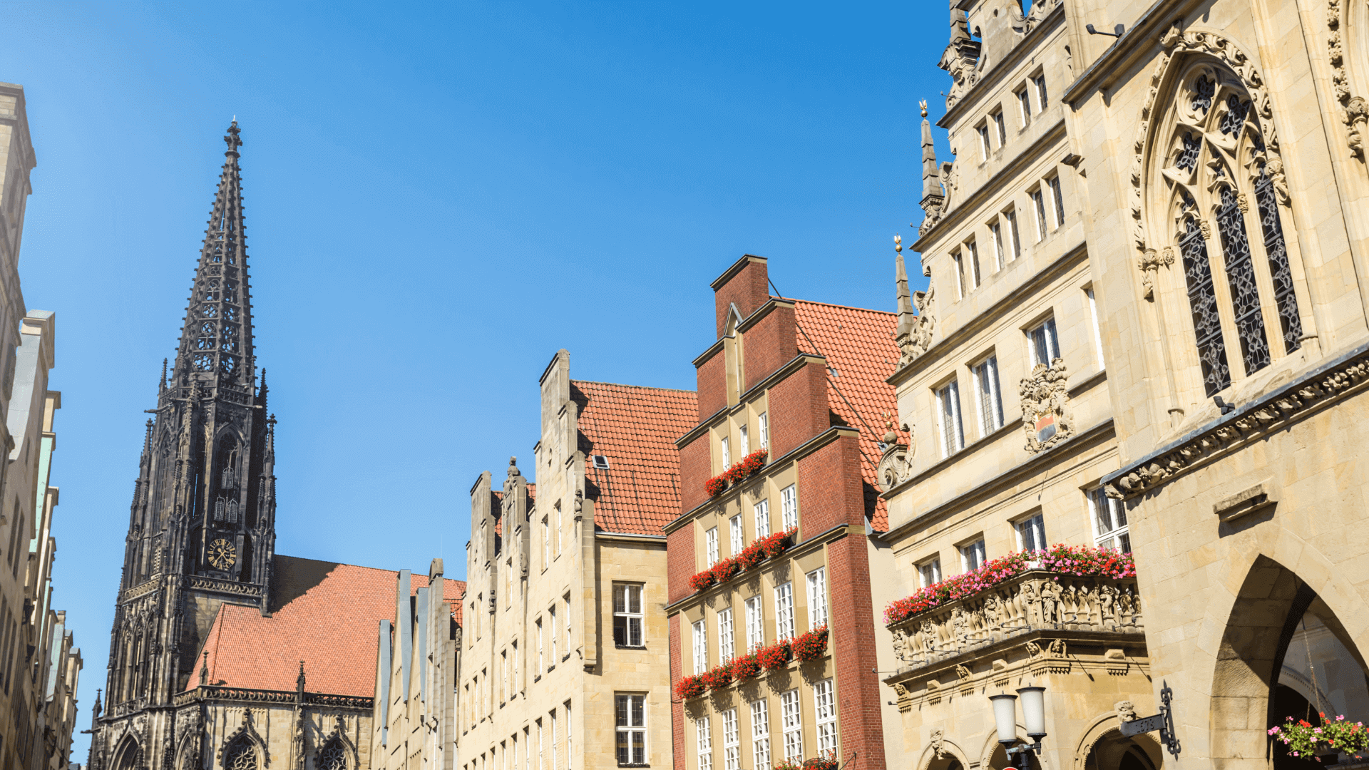 Historische Gebäude in Münster mit einem hohen Kirchturm im Hintergrund unter klarem Himmel.