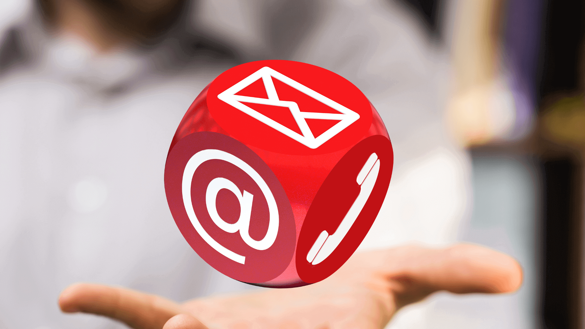 Roter Würfel mit einem Briefsymbol und einem Telefonsymbol in der Luft über einer Hand.