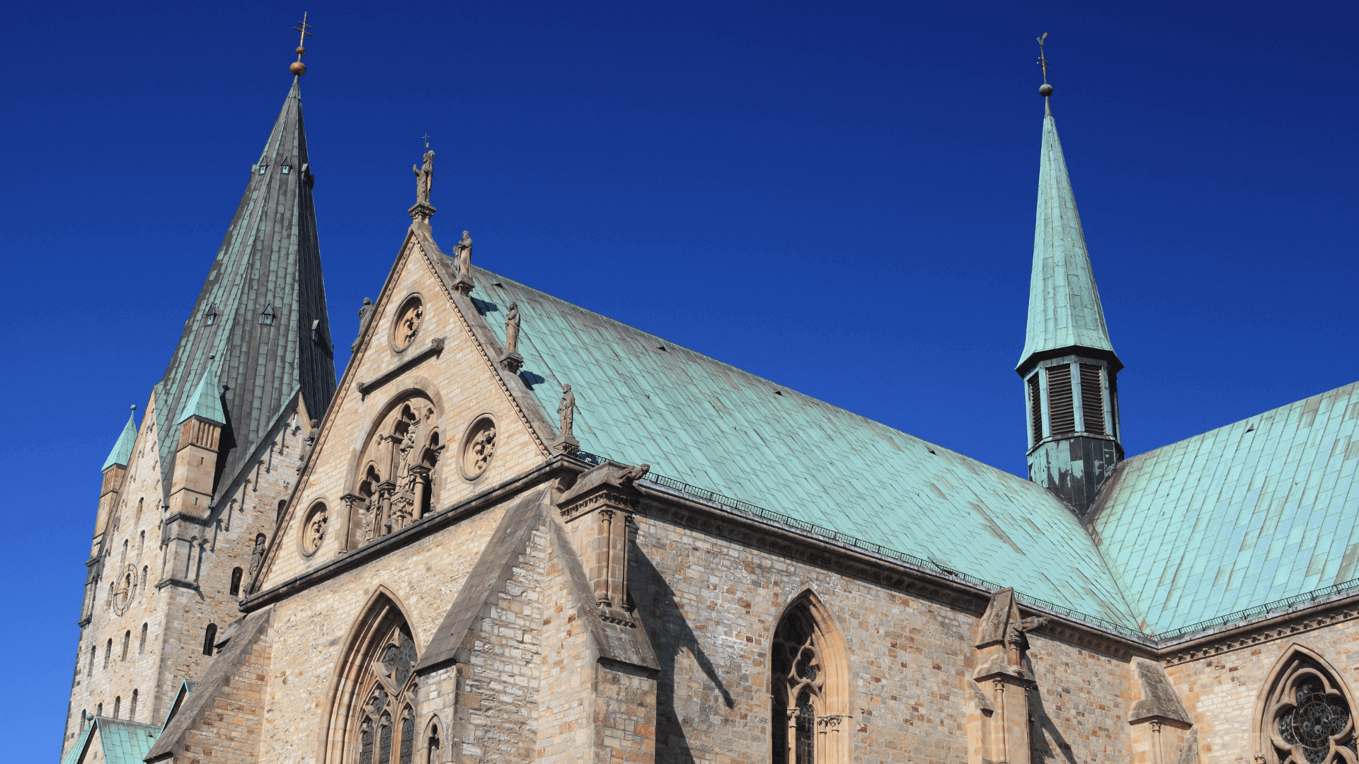 Detailansicht einer Kirche mit zwei spitzen Türmen und einem Kupferdach unter klarem blauen Himmel.