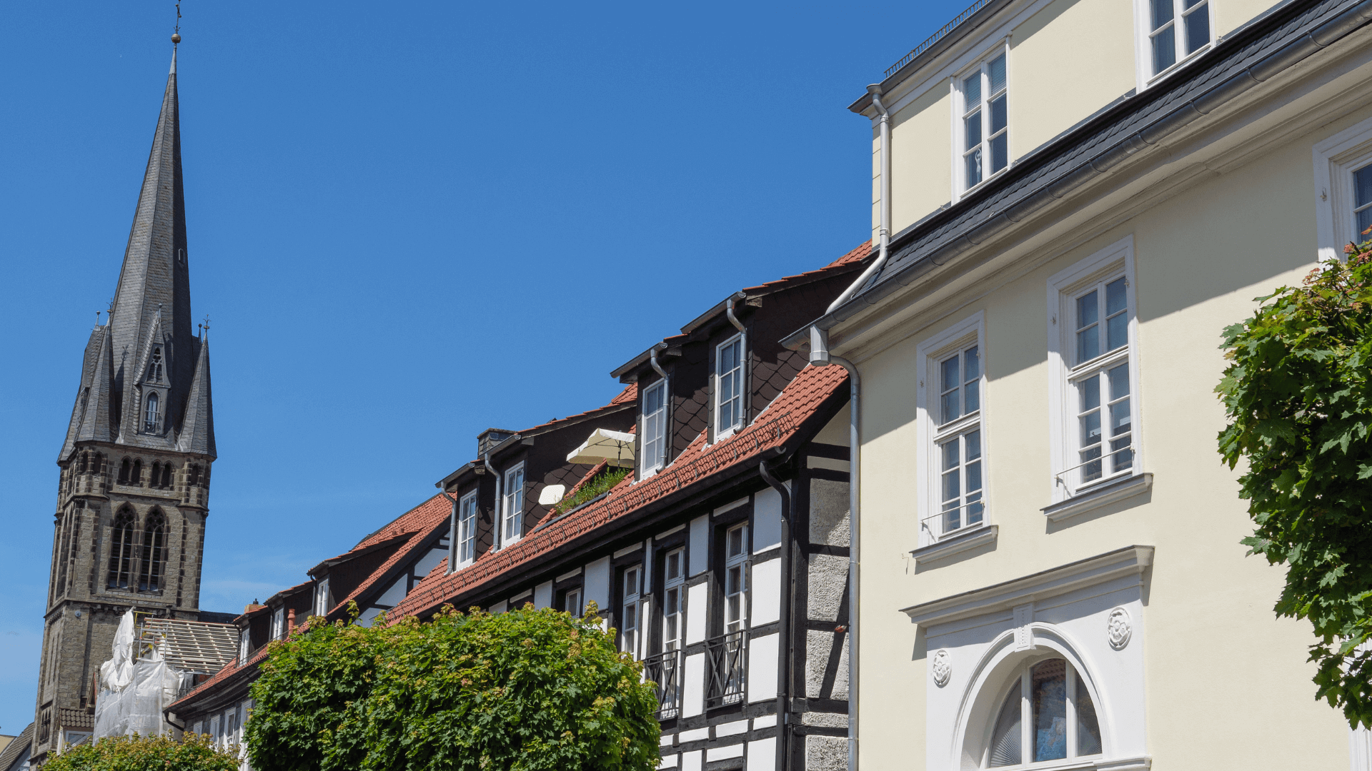 Stadtansicht mit einem hohen Kirchturm und historischen Gebäuden in Detmold unter blauem Himmel.