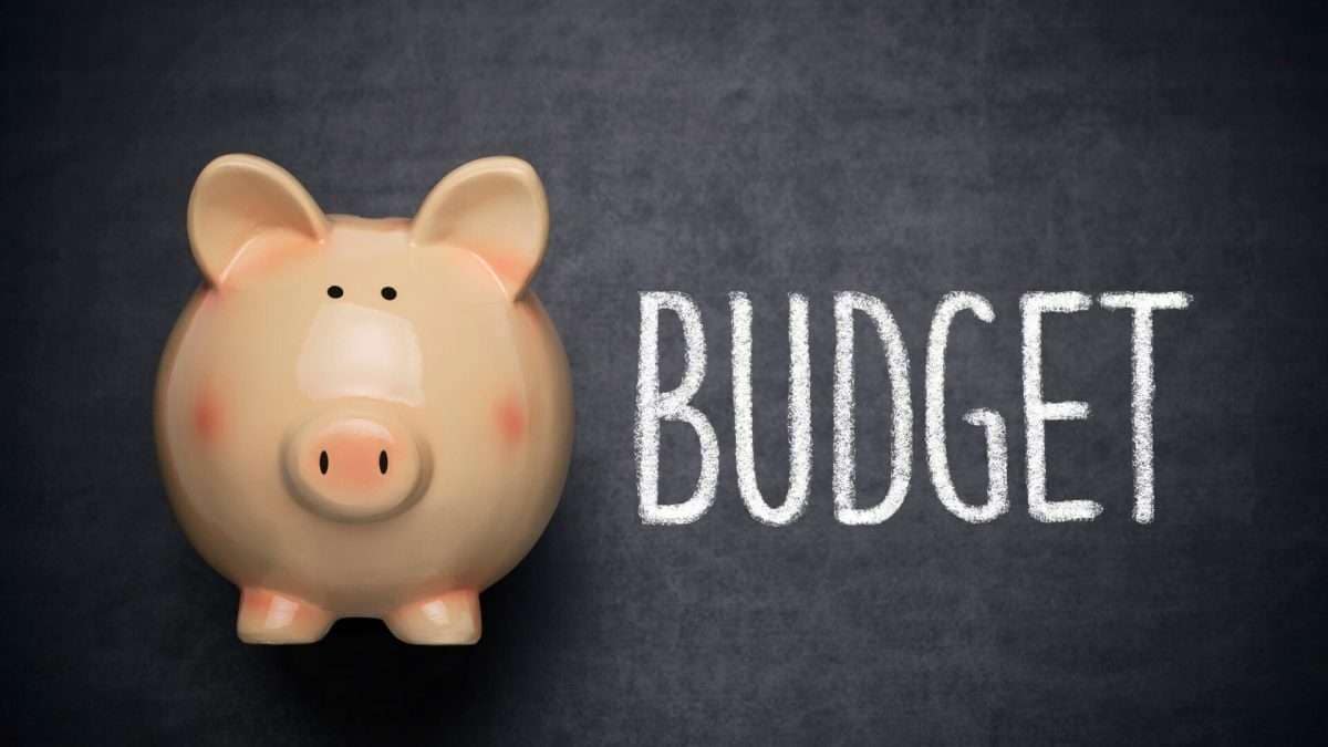 Ein Sparschwein aus Keramik mit dem Wort 'Budget' in Kreide auf einer Tafel.