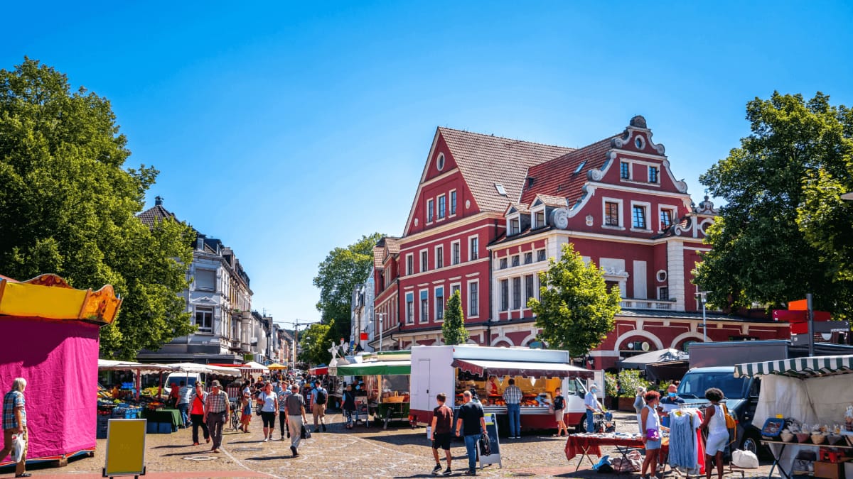 Marktplatz in Bergisch Gladbach mit Ständen und einem historischen Gebäude im Hintergrund.