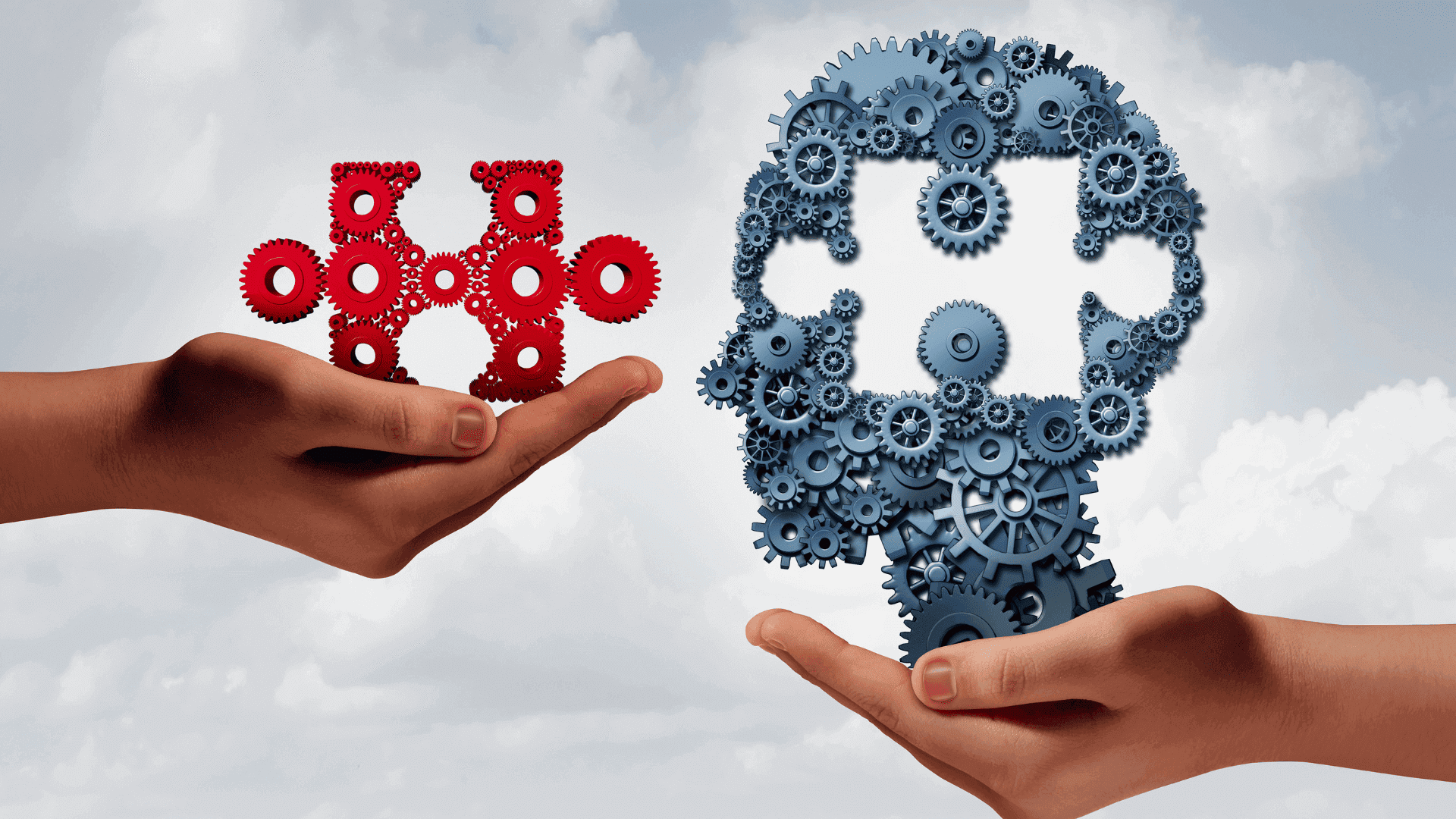 Zwei Hände halten rote und graue Zahnräder in Form von Puzzle-Teilen, die zusammenpassen.