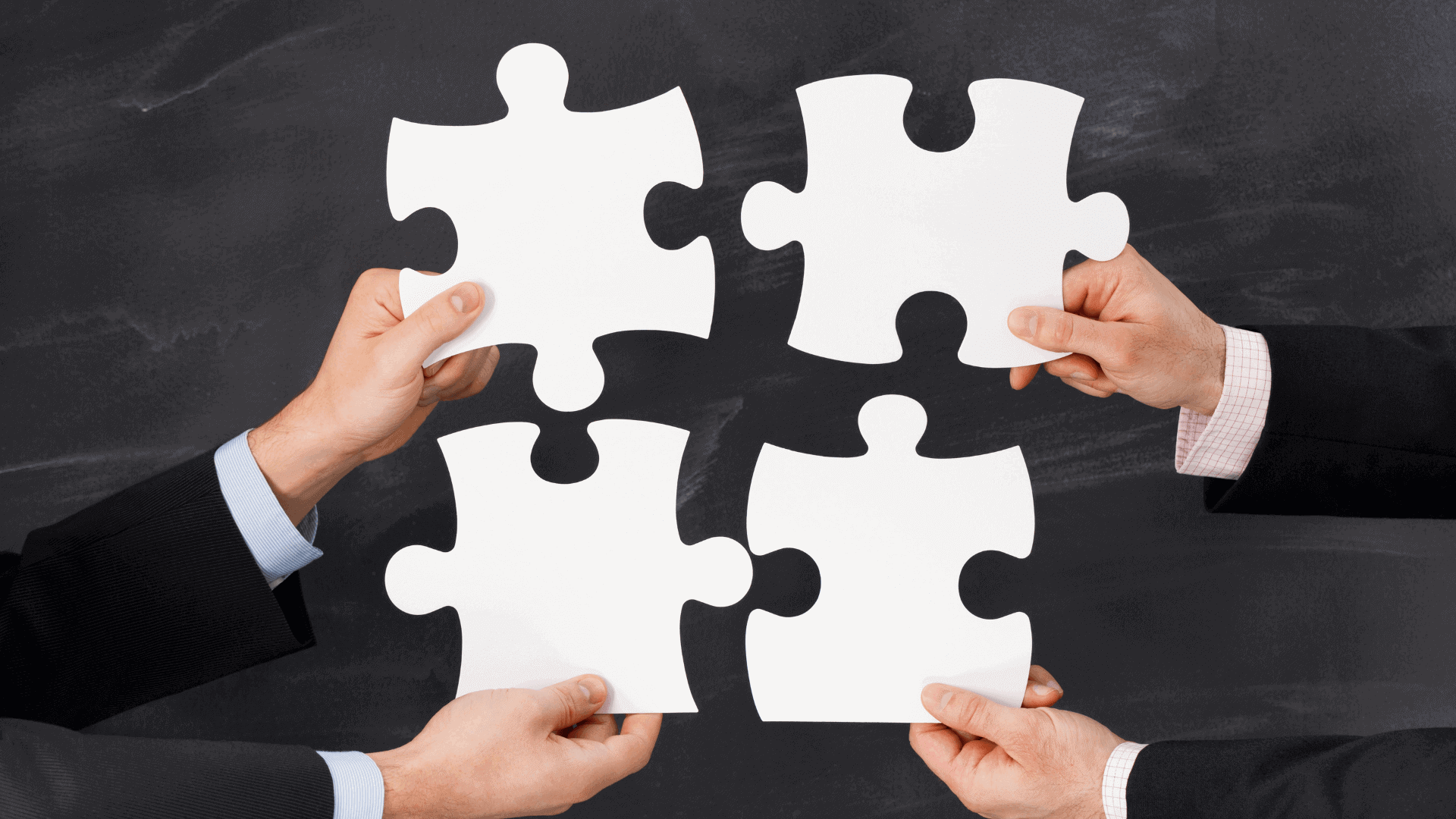 Vier Hände halten leere Puzzlestücke in einem geschäftlichen Umfeld.