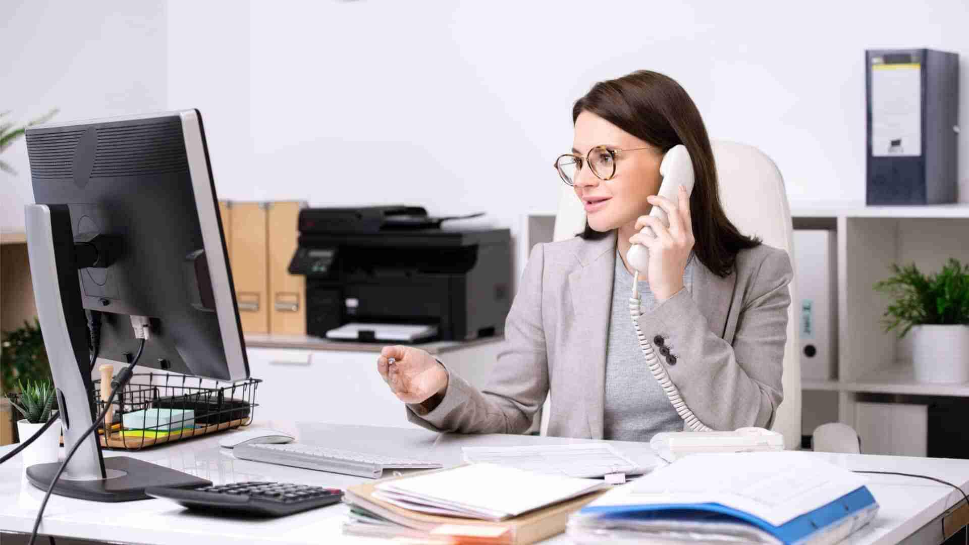 Frau mit Brille spricht am Telefon, während sie an einem Computer arbeitet.