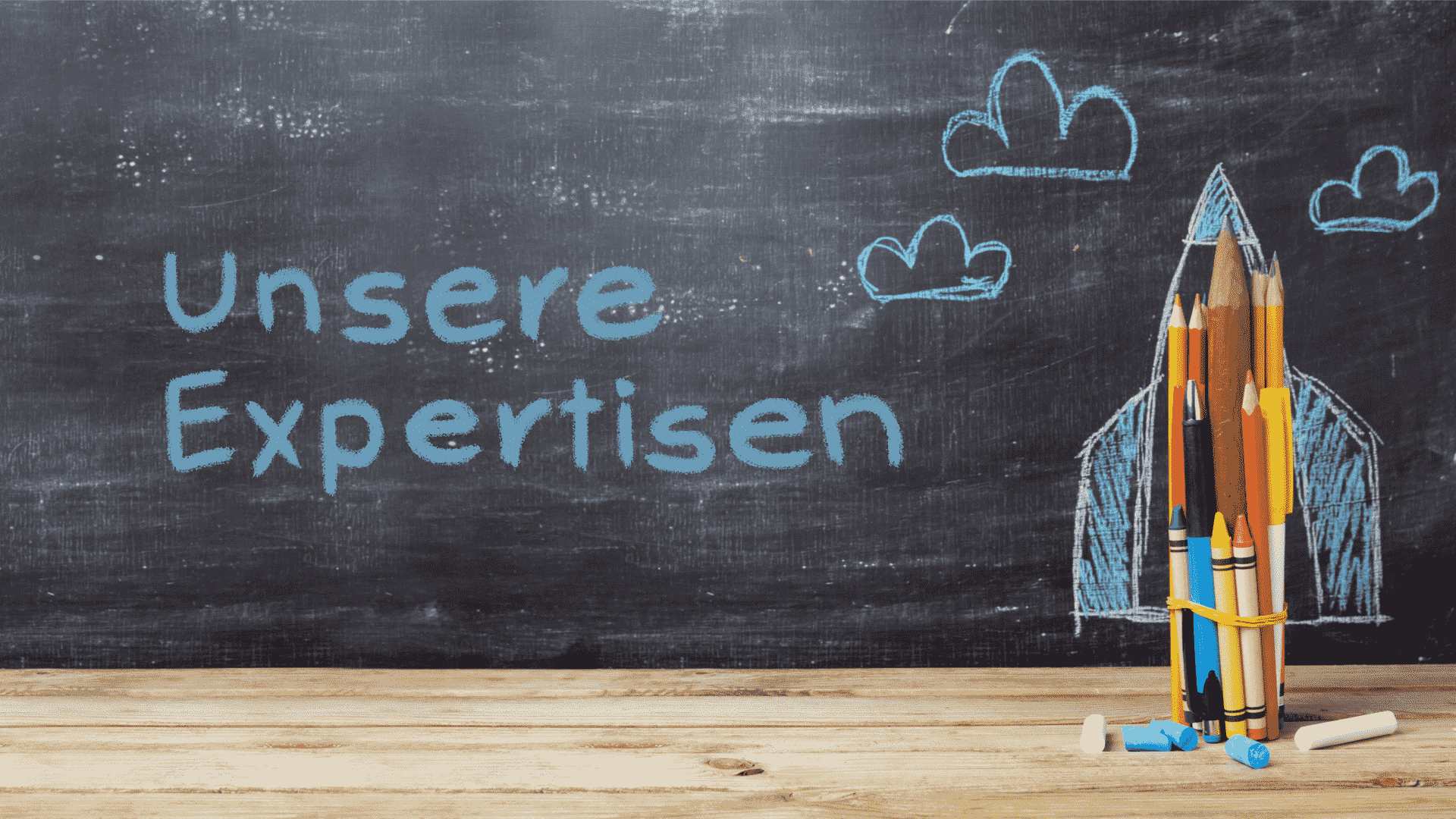 Buntstifte und Kreide auf einer Tafel mit der Aufschrift 'Unsere Expertisen'.