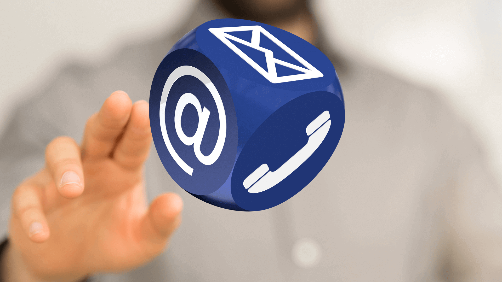 Blauer Würfel mit Symbolen für E-Mail, Telefon und Internetkommunikation in der Luft gehalten.