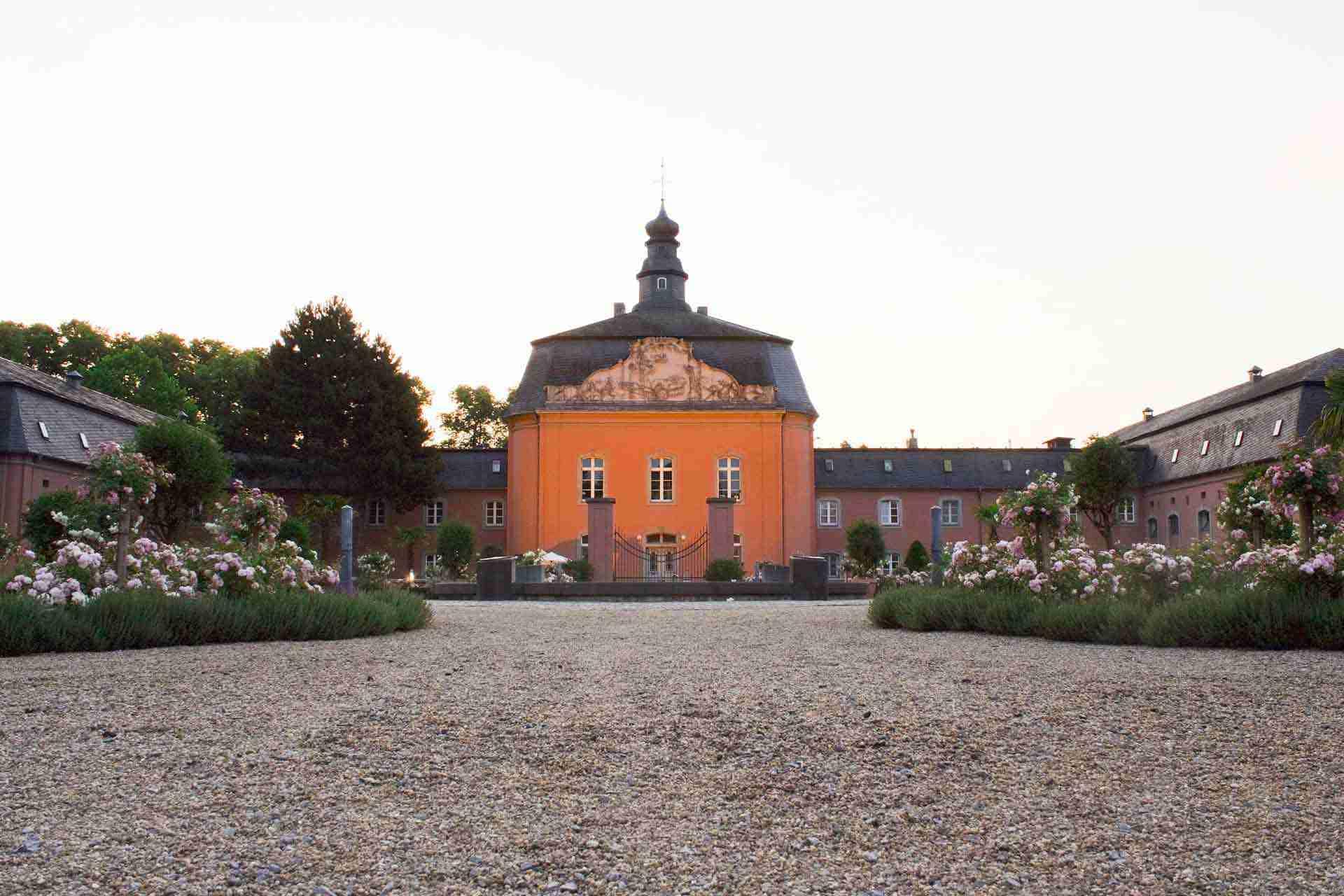 Schloss Mönchengladbach mit orangefarbener Fassade und Gartenanlagen im Vordergrund.