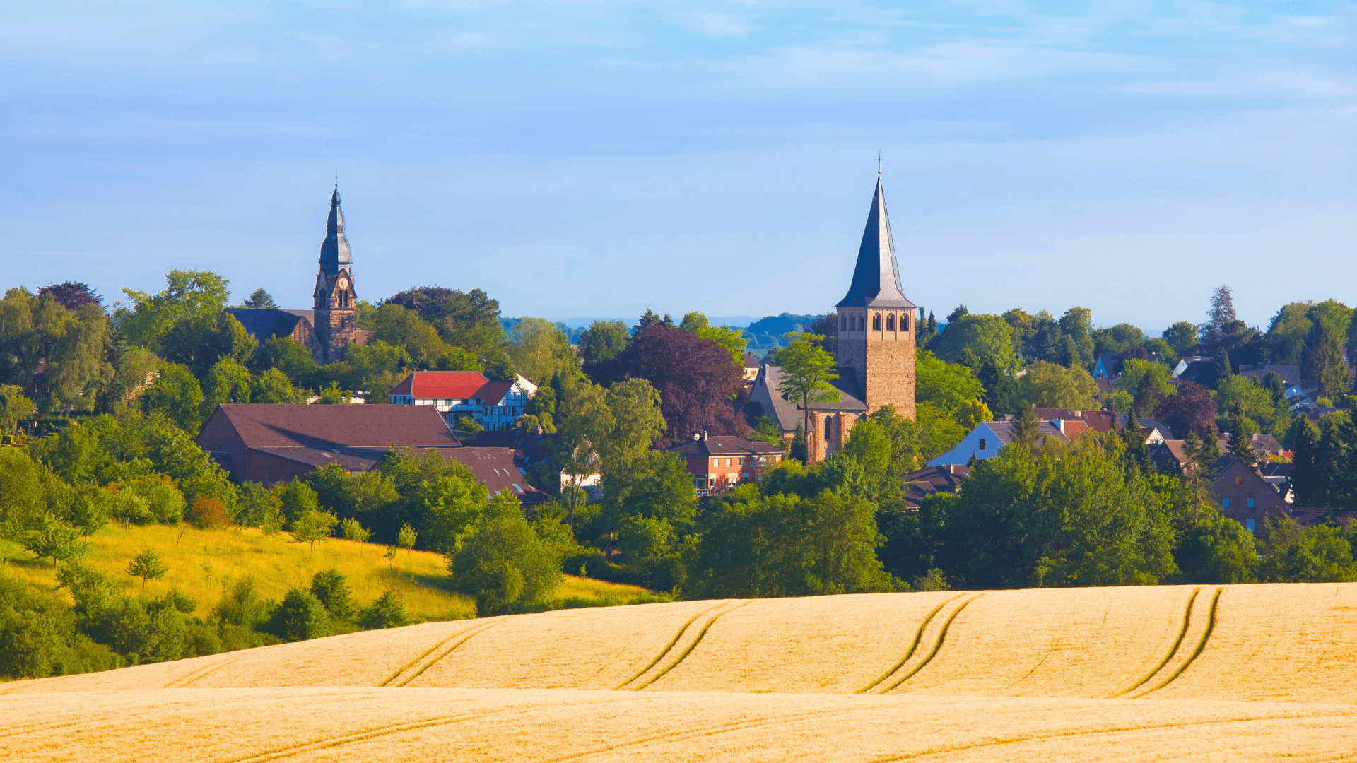 Landschaft mit Feldern und zwei Kirchtürmen in Ratingen, Deutschland, umgeben von Bäumen und Wiesen.