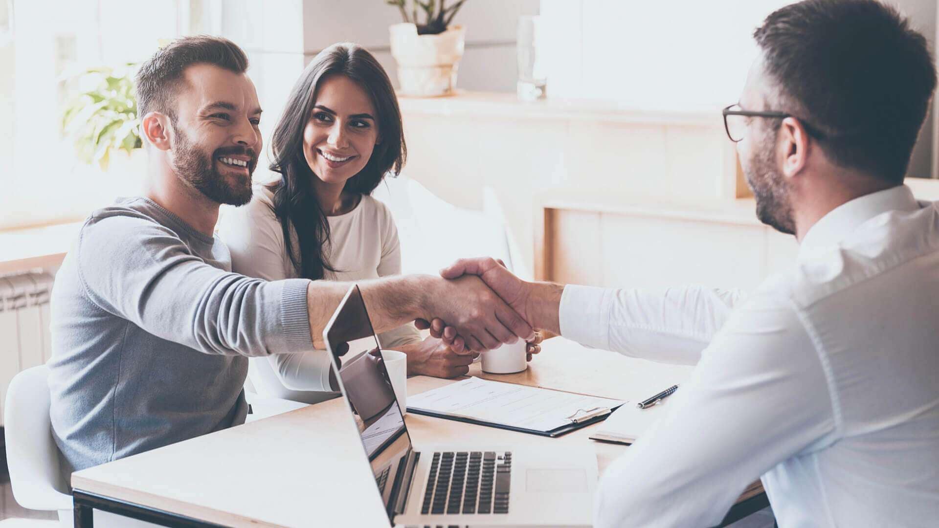 Drei Personen in einem Beratungsgespräch, ein Mann schüttelt einem anderen Mann die Hand.