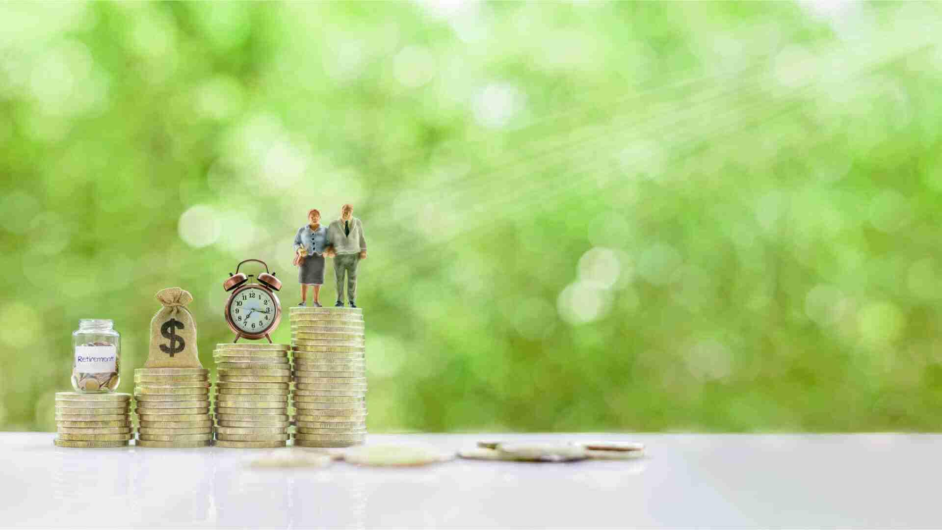 Zwei kleine Figuren stehen auf einem Stapel von Münzen neben einer Uhr und einem Sparschwein.