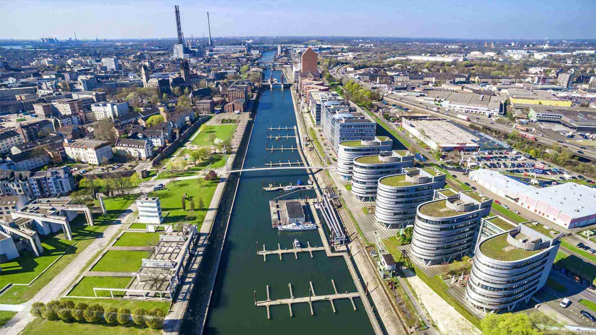 Luftaufnahme des Duisburger Hafens mit Wasserwegen und modernen Gebäuden entlang des Ufers.