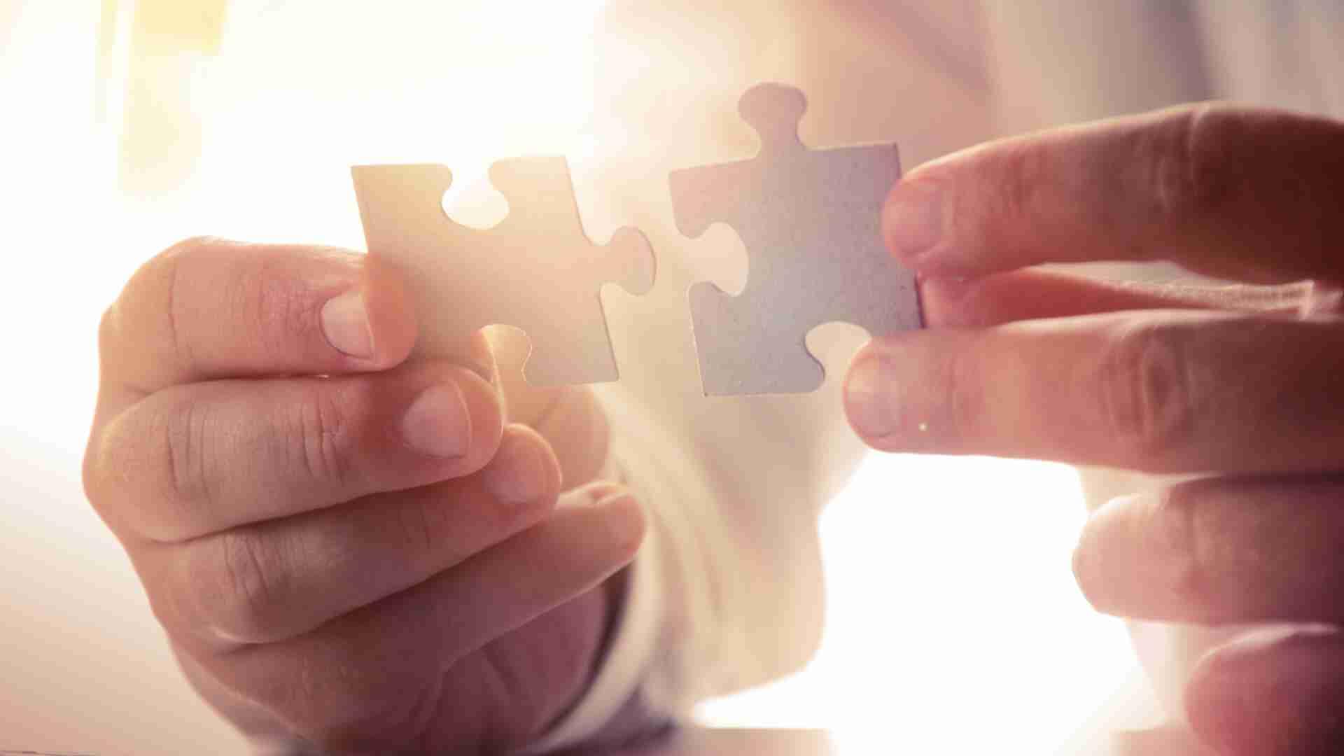Zwei Puzzlestücke werden von einer Hand gehalten, die im Licht gehalten werden.