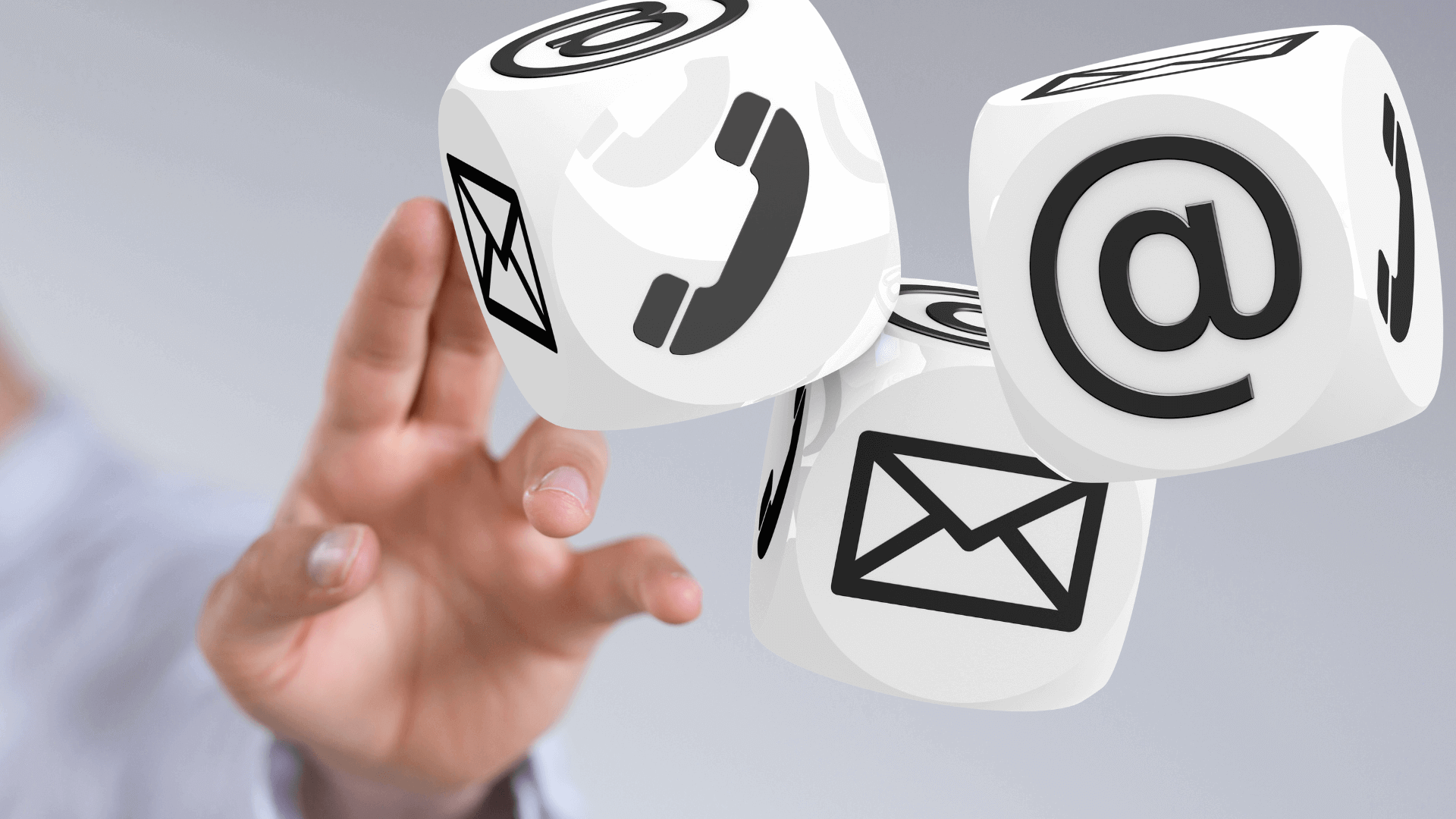 Drei Würfel mit Symbolen für Telefon, E-Mail und Kontaktmöglichkeiten in der Hand einer Person.